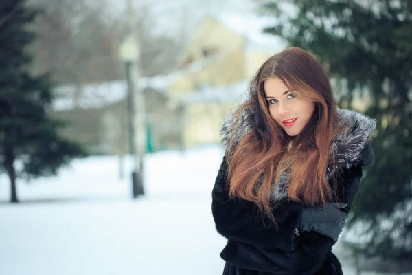 Szép mosolygó lány, háttérben a havas fák. Téli portré. kabát, kapucnival — Stock Fotó