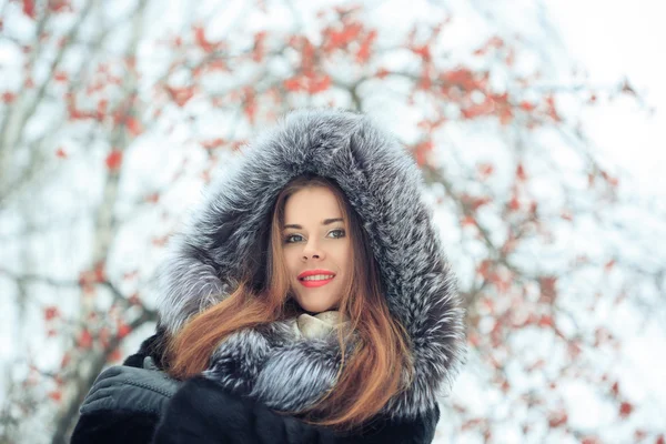 Krásná usměvavá dívka na pozadí zasněžených stromů. Zimní portrét. kabát s kapucí — Stock fotografie