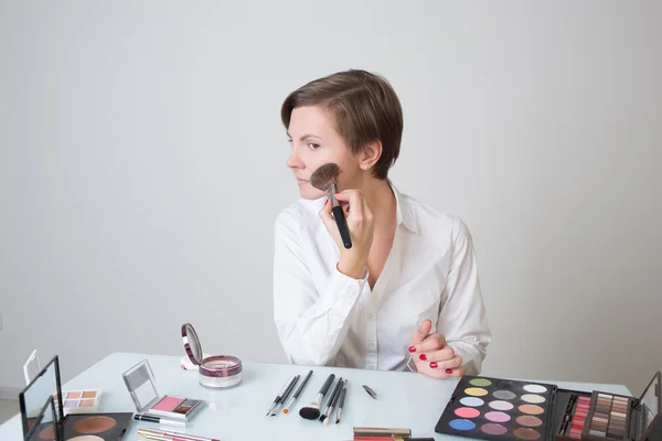 La donna adulta spaccia cosmetici sul viso. siede al tavolo . — Foto Stock