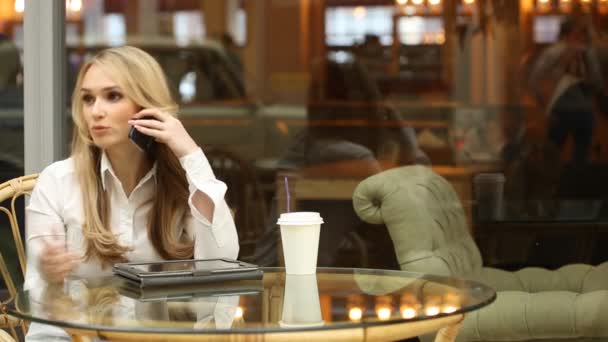 Una chica hablando por teléfono en un café. saludando con la mano. esperando amigos — Vídeo de stock