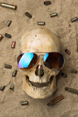 skull lying in the sand, scattered rifle and pistol cartridges. concept of war clipart