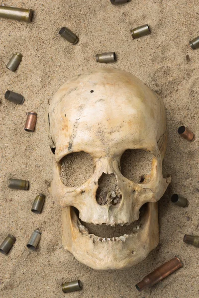 Crâne couché dans le sable, fusil éparpillé et cartouches de pistolet. concept de guerre — Photo