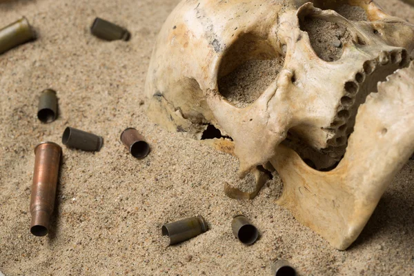 Crânio deitado na areia, espingarda espalhada e cartuchos de pistola. conceito de guerra — Fotografia de Stock