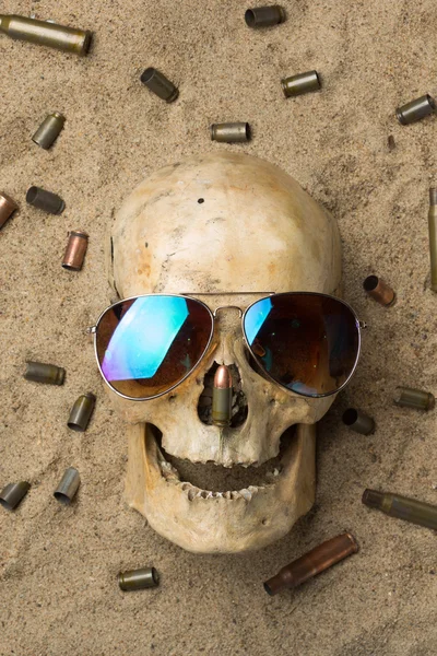 Skull lying in the sand, scattered rifle and pistol cartridges. concept of war — Stock Photo, Image