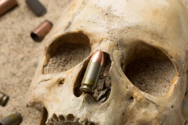 Crânio deitado na areia, espingarda espalhada e cartuchos de pistola. conceito de guerra — Fotografia de Stock