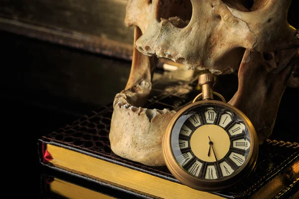 Cráneo humano en un libro al lado del reloj. concepto de magia negra —  Fotos de Stock