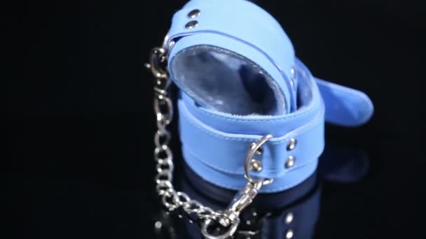 Голубые кожаные наручники на черном фоне. секс-игрушка — стоковое видео
