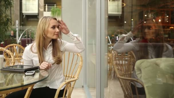 Mädchen glättet ihr Haar in einem Café, das aus dem Fenster schaut — Stockvideo