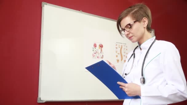 Doktor vyplňuje noviny. dívka v bílém kabátě s stetoskoborem píše na tabletu — Stock video