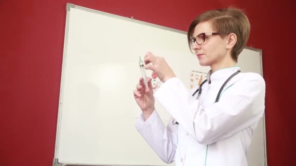 Doctora en bata de laboratorio con estetoscopio muestra una jeringa — Vídeos de Stock