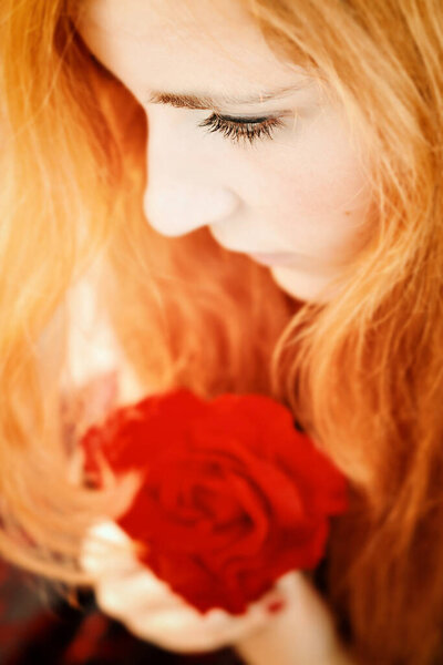 Close-up portrait of beautiful redhead woman with red rose
