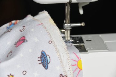 Bir kadın dikiş makinesine dikiş dikiyor, kumaşın kenarını zikzak ile işliyor, bir terzi kendini izole etmek için bebek bezi dikiyor..