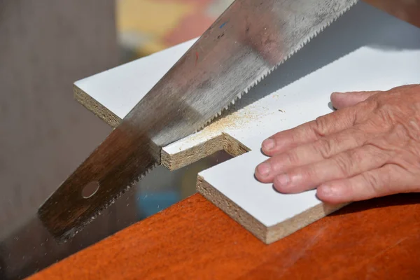 街上的一个人修理架子 用锯子把多余的部分从木板上剪下来 再用文件处理 在自我隔离时 一个男人在家里修理家具 — 图库照片