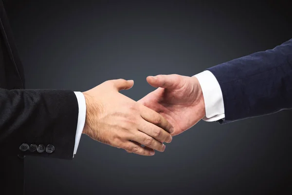 Handshake of two businessmen on a black wall background, partnership concept, close up — Stock Photo, Image