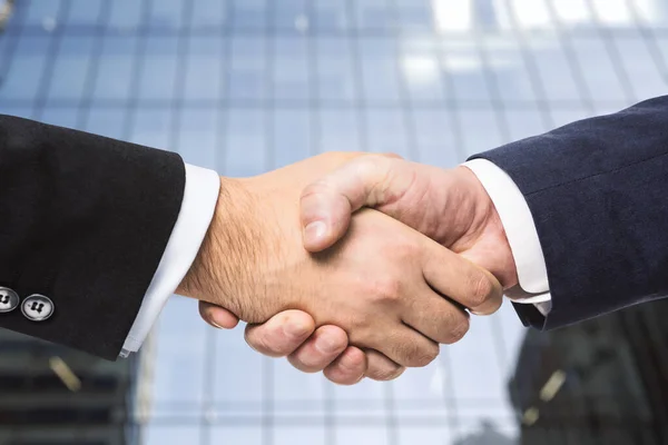 Рукопожатие двух бизнесменов на фоне офисных окон, концепция партнерства, крупный план — стоковое фото