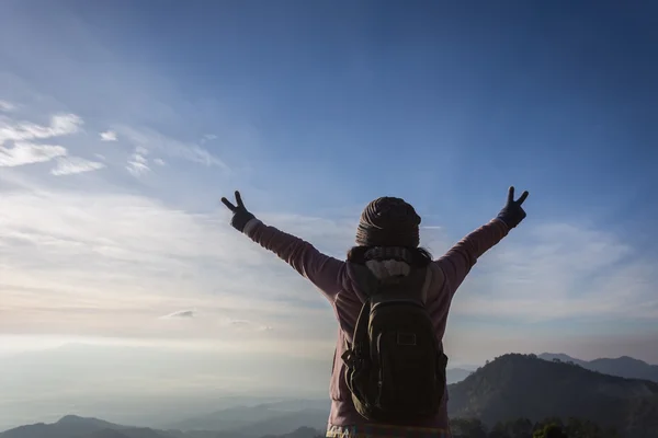 Woman with backpack standing on top of a mountain with raised ha — Stock Photo, Image