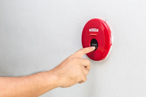 Mano con el dedo presionando alarma de fuego rojo en la pared — Foto de Stock