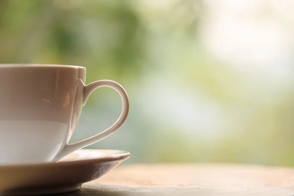 Біла чашка кави на столі в саду з розмитим світлом боке — стокове фото