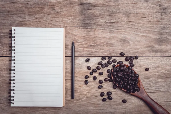 Kaffebönor och och fodrade papper på träbord ovanifrån — Stockfoto