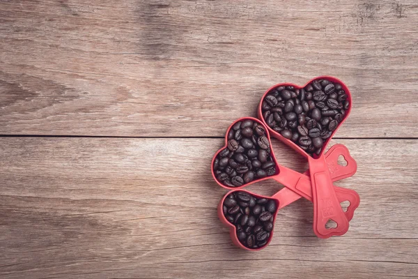 Kaffeebohnen in rotem Herzen Plastikbecher auf hölzerner Tischplatte Ansicht — Stockfoto