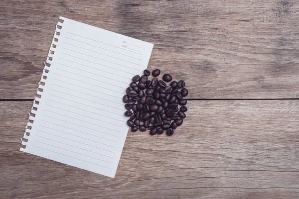 Kaffebönor och och fodrade papper på träbord ovanifrån — Stockfoto