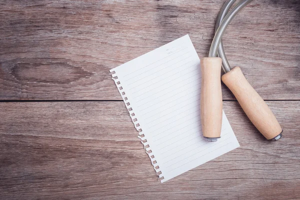 Skipping rope and lined paper on wooden table top view — Stock Photo, Image