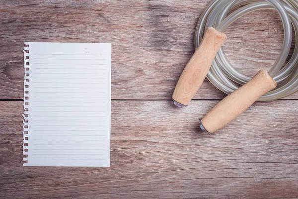 Skipping rope and lined paper on wooden table top view — Stock Photo, Image