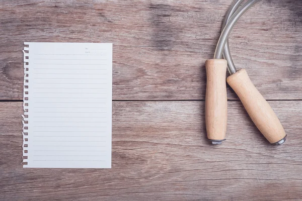 Skipping rope and lined paper on wooden table top view — Stock Photo, Image