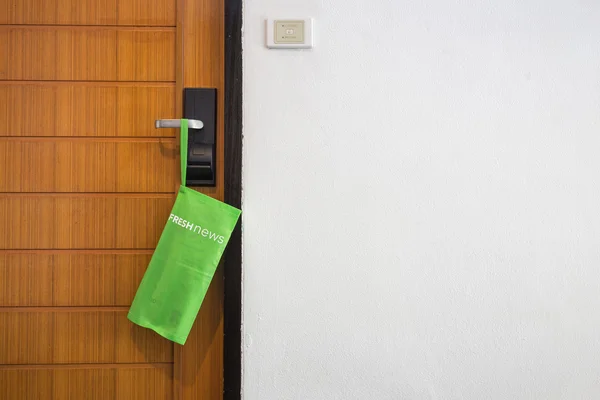 Bolsa verde com jornal pendurar na porta do hotel — Fotografia de Stock