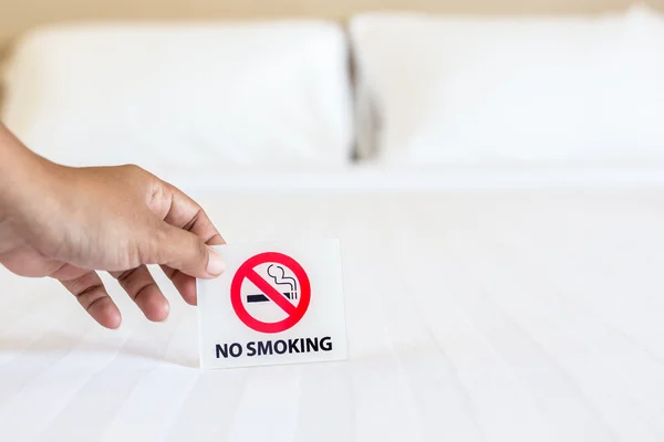 Mano sosteniendo NO Fumar signo en la cama en la habitación del hotel — Foto de Stock