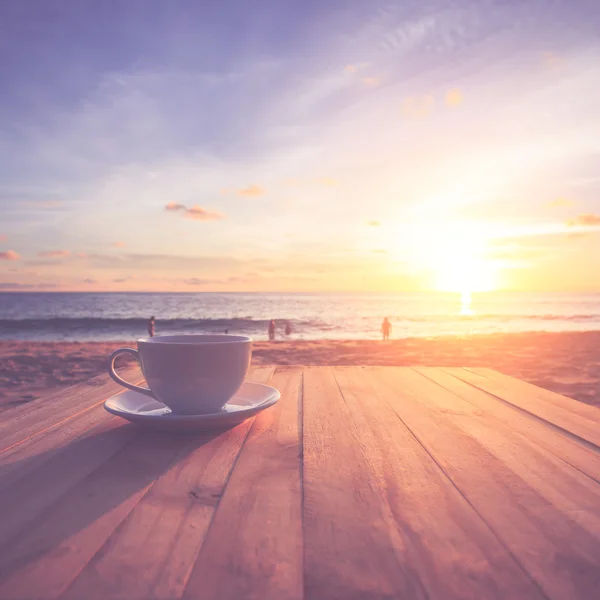 Kaffekopp på bord av trä på solnedgången eller sunrise beach — Stockfoto