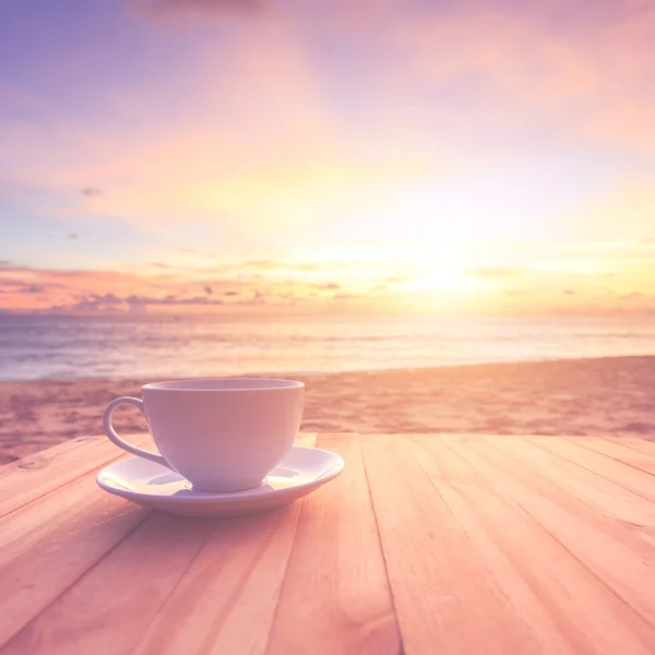 Xícara de café na mesa de madeira ao pôr do sol ou ao nascer do sol praia com lente fl — Fotografia de Stock