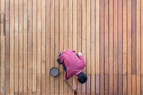 Un homme peignant la terrasse extérieure de la piscine en bois, vue de dessus — Photo