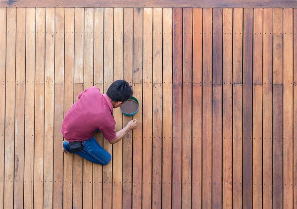 Un homme peignant la terrasse extérieure de la piscine en bois, vue de dessus — Photo