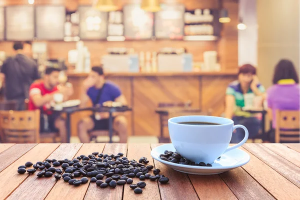 Weiße Kaffeetasse und Kaffeebohnen auf Holztisch mit verschwommenem Bac — Stockfoto