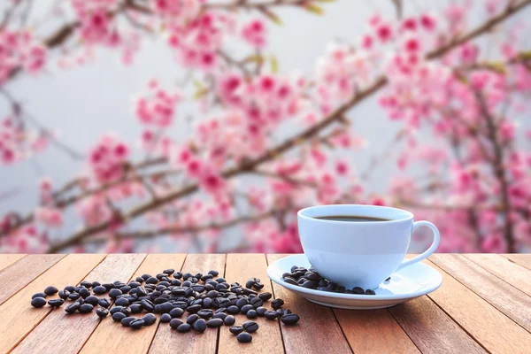 Weiße Kaffeetasse und Kaffeebohnen auf Holztisch mit verschwommenem Bac — Stockfoto