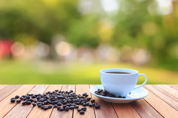 Weiße Kaffeetasse und Kaffeebohnen auf Holztisch mit verschwommenem Bac — Stockfoto