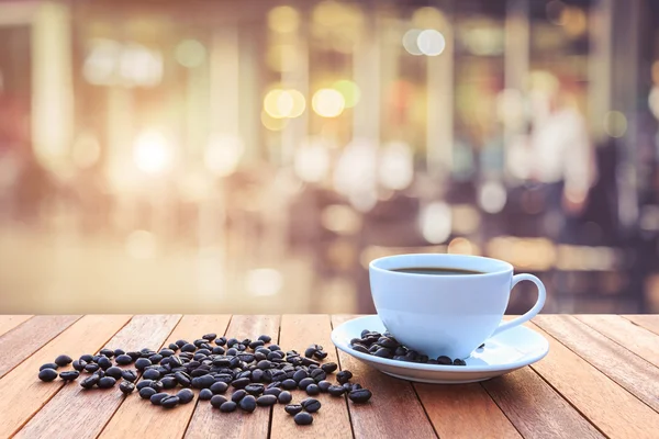 Weiße Kaffeetasse und Kaffeebohnen auf Holztisch mit verschwommenem Bac — Stockfoto