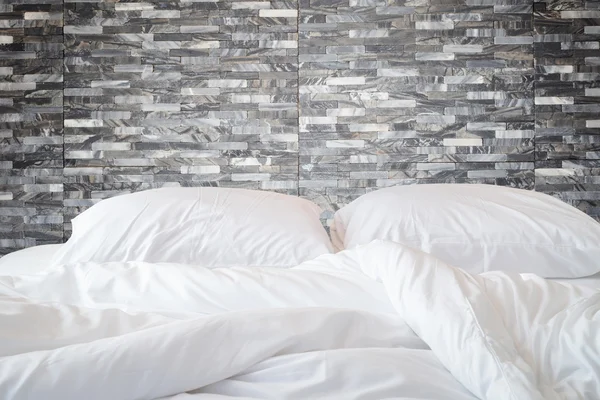 White bedding sheets and pillow on natural stone wall room backg — Stock Photo, Image