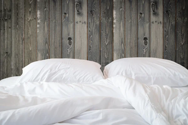 White bedding sheets and pillow on wooden wall room background,
