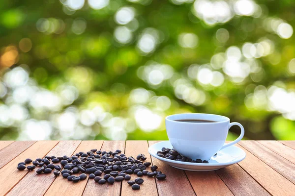 Weiße Kaffeetasse und Kaffeebohnen auf Holztisch mit verschwommenem Bac — Stockfoto