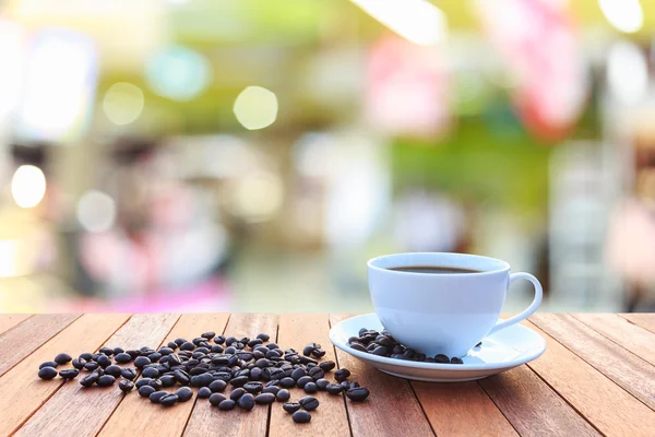 Weiße Kaffeetasse und Kaffeebohnen auf Holztisch mit verschwommenem Bac — Stockfoto