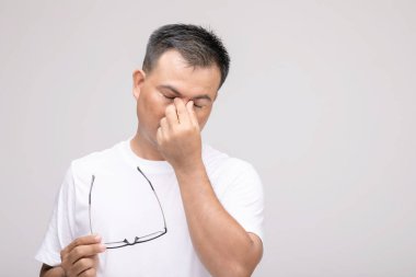 Göz tahriş konsepti: Asyalı bir adamın göz duruşu, yorgunluk ve gözündeki rahatsızlık portresi. Stüdyo çekimi gri arkaplanda izole edildi