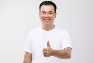 Taylandlı adamın portresi, el başparmağı yukarıda, stüdyoda, gri arka planda.