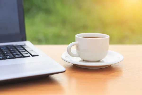 Cierre la taza de café y el portátil en la mesa por la mañana — Foto de Stock