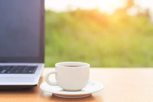 Zblízka šálek kávy a laptop na stole ráno — Stock fotografie