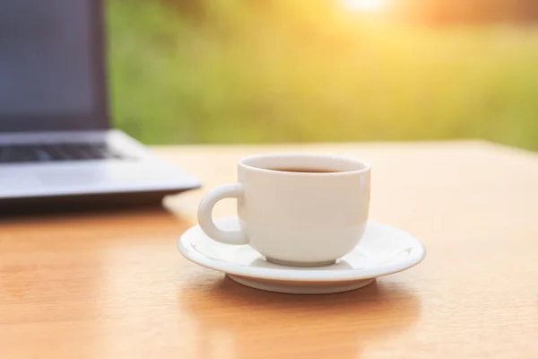 Cierre la taza de café y el portátil en la mesa por la mañana —  Fotos de Stock