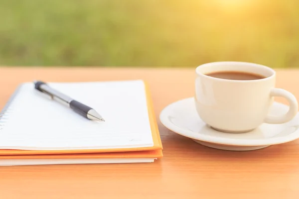 Feche a xícara de café e caderno na mesa — Fotografia de Stock