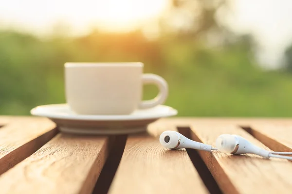 Cierra los auriculares y la taza de café en la mesa por la mañana — Foto de Stock