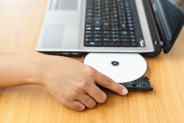 テーブルの上のノート パソコンに cd を挿入する手 — ストック写真